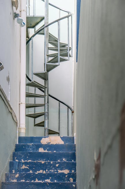 A narrow stone staircase with about ten steps ascending between two multi-storey buildings in a dense urban area. The building on the left has a white façade with decorative architectural details and